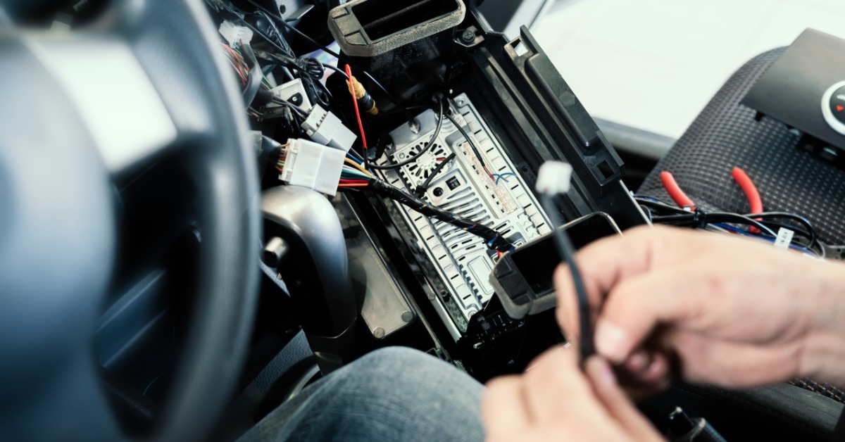 A person using their bare hands to work on connectors inside a car. The person is sitting in the driver’s seat.